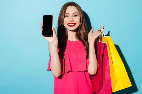 Felice giovane donna bruna in possesso di telefono cellulare e borse della spesa — Foto Stock
