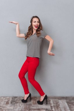 Mutlu genç bayan gri duvardan ayakta ve müzik dinlemek