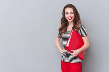 Mutlu genç bayan gri duvardan ayakta ve klasör holding