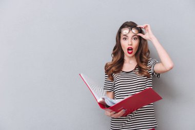 Gri duvardan ayakta ve klasör tutan şok genç bayan