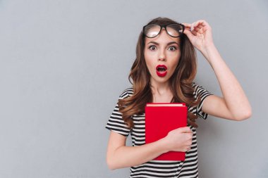 Şok genç bayan kitap gri duvardan ayakta.