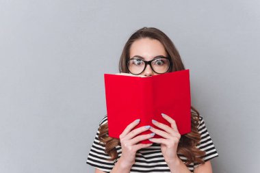 Sürpriz genç bayan kitap gri duvardan ayakta