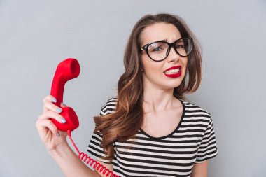 Karışık genç bayan telefon tutarak gri duvardan ayakta.