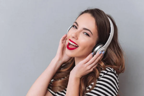 Jovencita feliz parada sobre la pared gris y escuchando música — Foto de Stock