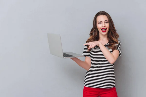 Jovem alegre de pé sobre a parede cinza e usando laptop — Fotografia de Stock