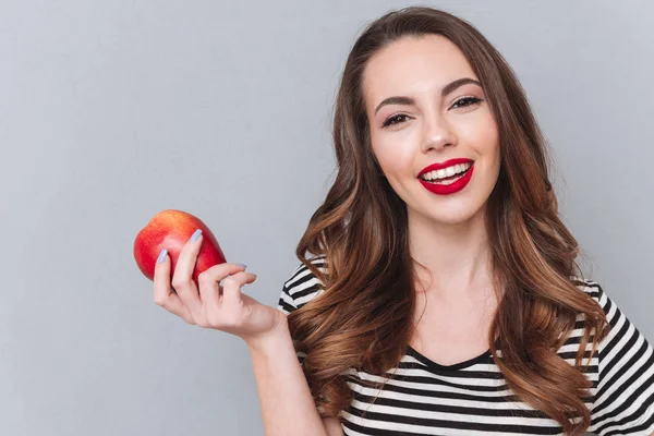 Feliz jovencita caminando sobre la pared gris y sosteniendo la manzana . —  Fotos de Stock