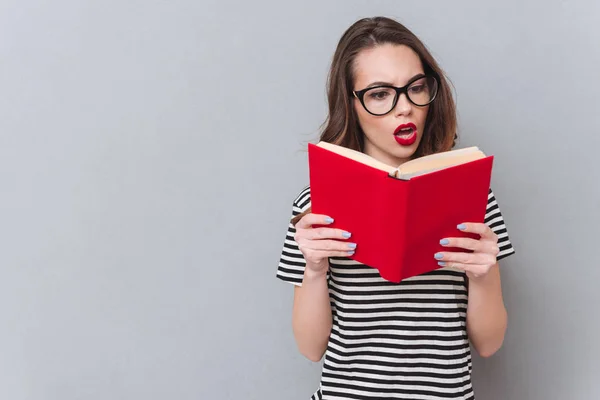 Confus jeune femme debout sur le mur gris livre de lecture . — Photo