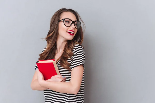 Glückliche junge Frau steht über grauer Wand und hält Buch — Stockfoto