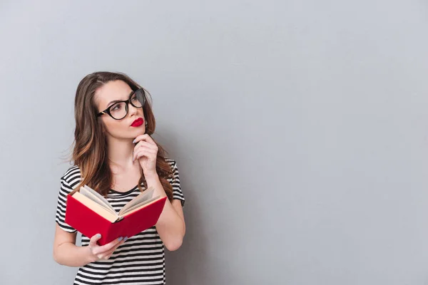 Denken jonge dame permanent over grijs muur lezen boek — Stockfoto