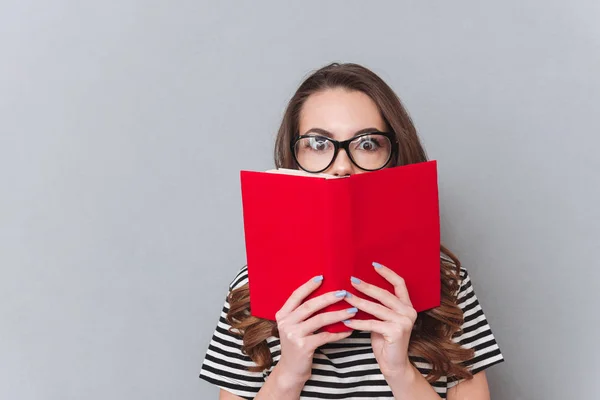 Sorprendido joven dama de pie sobre la pared gris sosteniendo libro —  Fotos de Stock