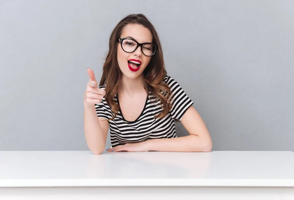 Glückliche junge Frau mit Brille sitzt über grauer Wand. — Stockfoto