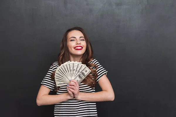 Feliz joven de pie sobre la pared gris y sosteniendo el dinero — Foto de Stock