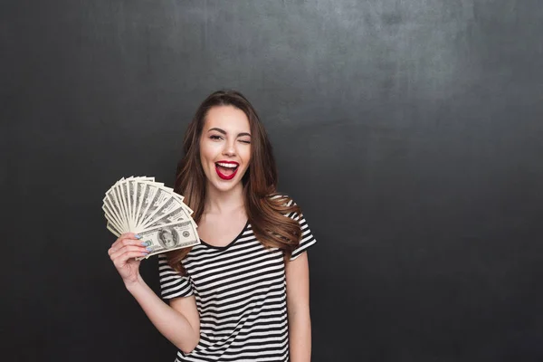 Happy young lady standing over grey wall and holding money — Stock Photo, Image