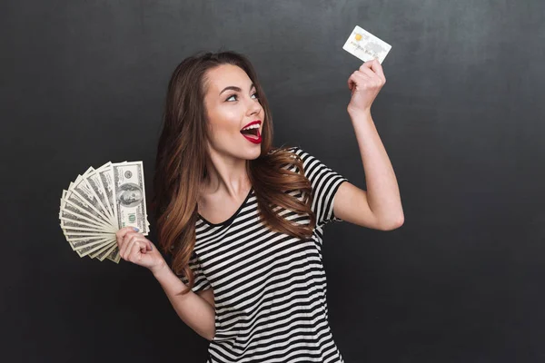 Jovencita sonriente sosteniendo dinero y tarjeta de débito en las manos — Foto de Stock