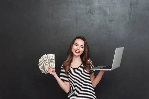 Χαμογελαστή γυναίκα που κρατά χρήματα και το φορητό υπολογιστή — Φωτογραφία Αρχείου