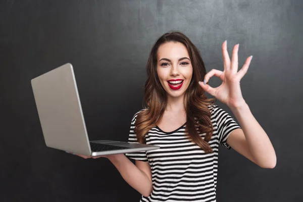 Sorrindo mulher segurando computador portátil e mostrando sinal ok — Fotografia de Stock