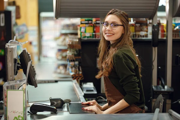 Fröhliche Kassiererin am Arbeitsplatz im Supermarkt. — Stockfoto