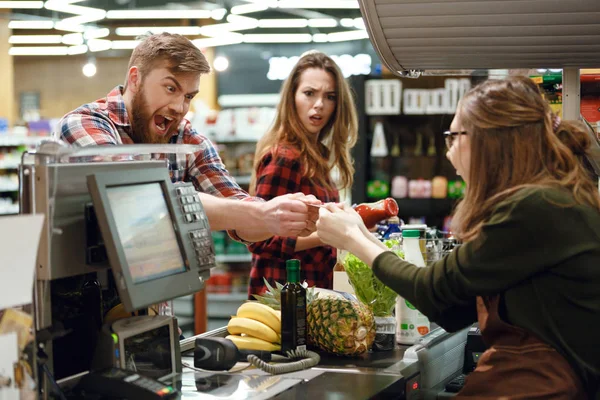 Angry young man doesn't give the credit card to cashier. — Stock Photo, Image