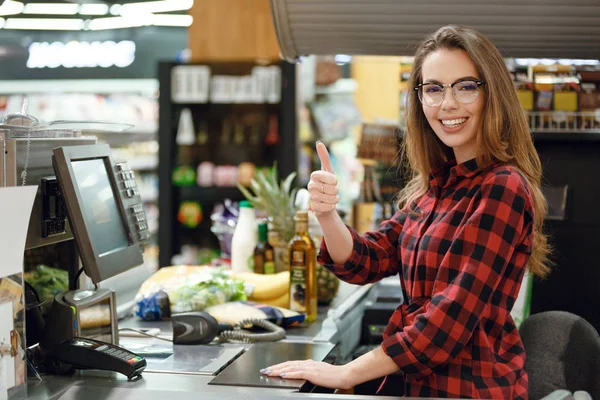 Vrolijke kassa vrouw op werkruimte duimen opdagen. — Stockfoto