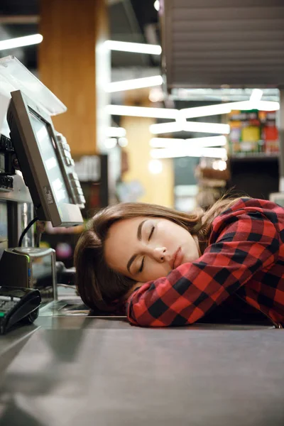 Cashier lady sleeping on workspace in supermarket shop.