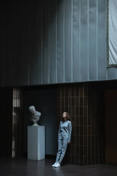 Kvinnan lutar sig mot en mörk vägg i ett konstgalleri — Stockfoto