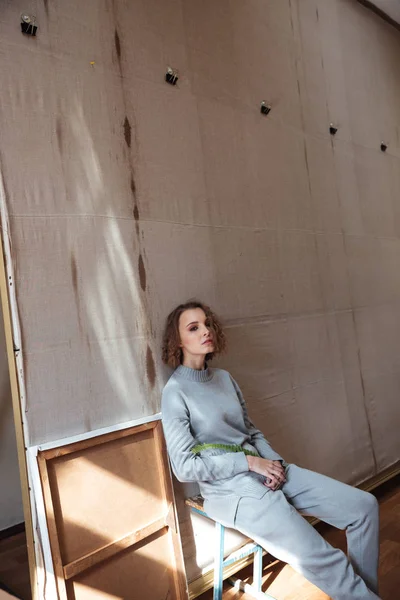 Woman sitting and leaning against a canvas backdrop — Stock Photo, Image