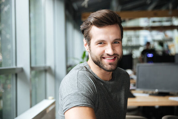 Handsome smiling young man sitting in office coworking.