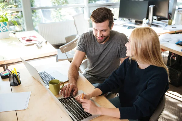 Lykkelige unge kolleger som sitter i kontorarbeid med bærbar datamaskin – stockfoto
