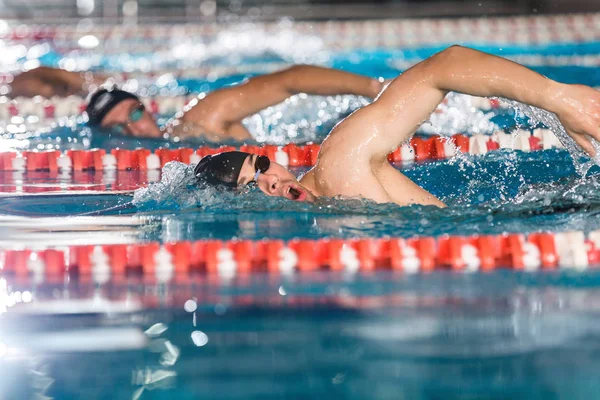 Trois nageurs masculins faisant style libre dans différentes voies de baignade — Photo
