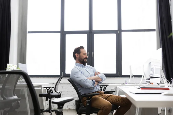 Зрілий бізнесмен сидить на стільці зі складеними руками — стокове фото