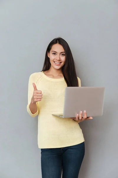 Feliz linda jovem segurando laptop e mostrando polegares para cima — Fotografia de Stock