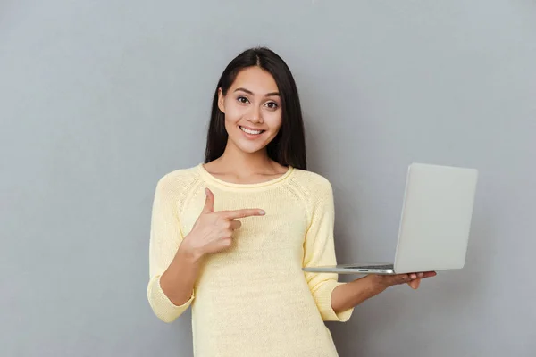 Sorridente attraente giovane donna che tiene e punta sul computer portatile — Foto Stock