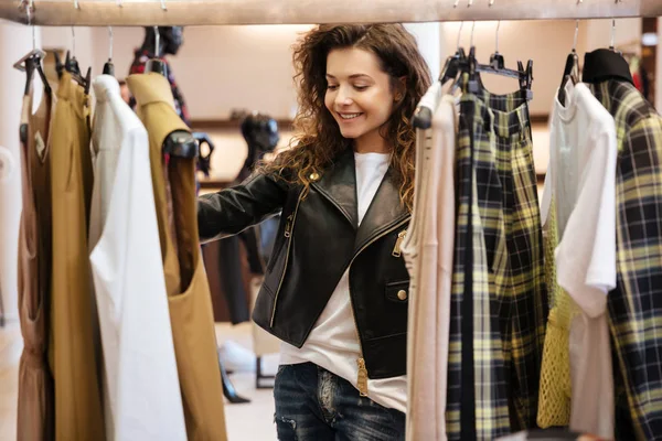 Cheerful curly young lady standing in women's clothing shop — Stock Photo, Image