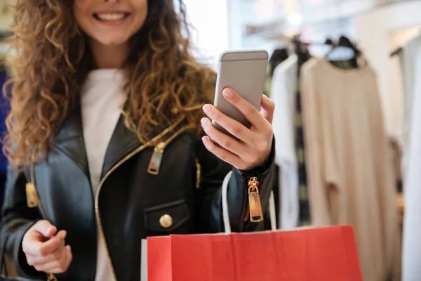 Beskuren bild av glada damen med shoppingkassar som håller telefonen. — Stockfoto