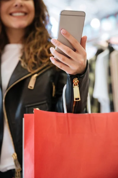 Beskuren bild av glada damen med shoppingkassar som håller telefonen. — Stockfoto