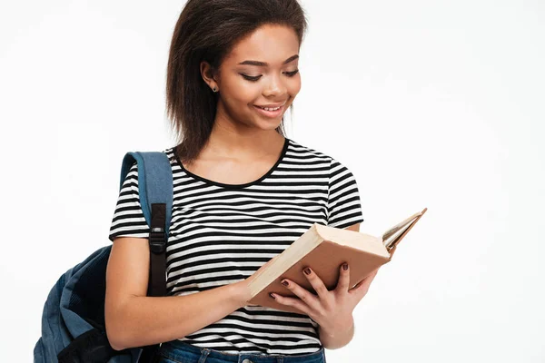 Sonriente afro-americana adolescente chica con mochila lectura libro —  Fotos de Stock