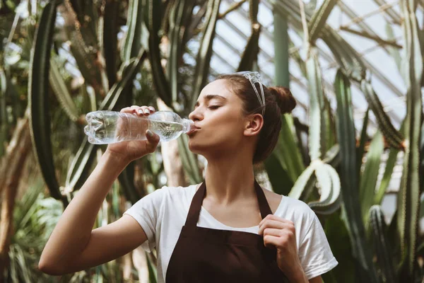 深刻な若い女性が立っている温室飲料水. — ストック写真
