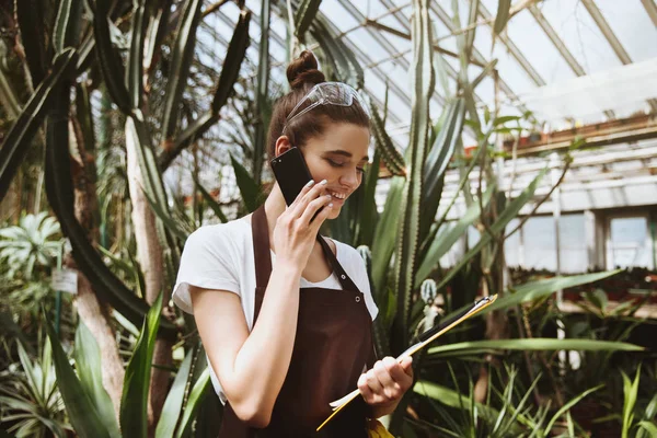 Šťastná mladá žena stojící ve skleníku mluví o telefonu — Stock fotografie