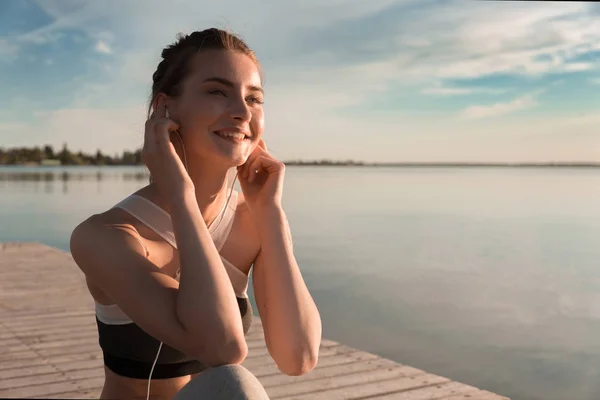 Leende sport dam på stranden Lyssna på musik med hörlurar — Stockfoto