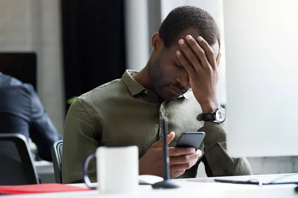 Расстроенный молодой африканский мужчина, читающий сообщение на мобильном телефоне — стоковое фото