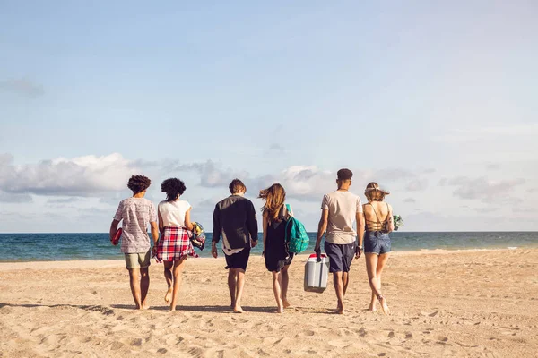 Молодые люди ходят по пляжу с кулер-боксом — стоковое фото