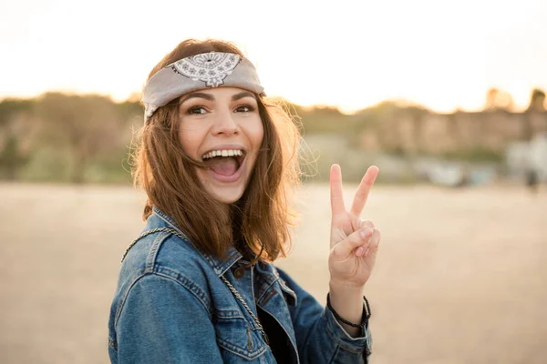 Счастливая молодая девушка показывает жест мира и смотрит в камеру — стоковое фото