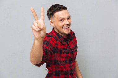 Mutlu genç adam barış hareketi gösterilen kameraya bakan.