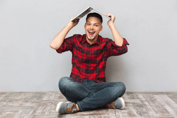 Cheerful young man in plaid sirt holding laptop over head — Stock Photo, Image