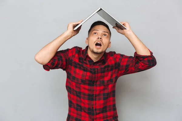 Cheerful young man in plaid sirt holding laptop over head — Stock Photo, Image