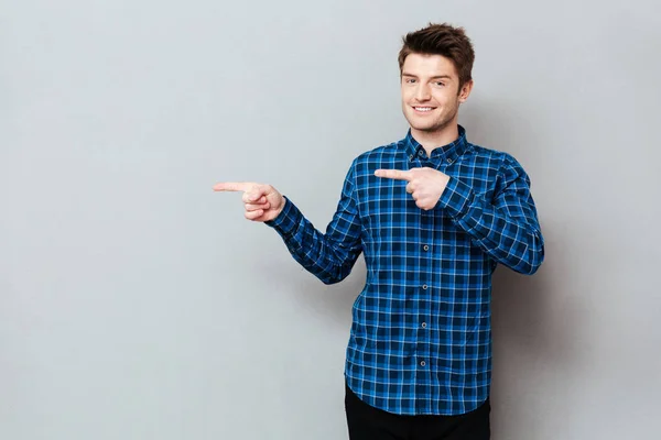 Attractive happy young man standing over grey wall and pointing — Stock Photo, Image