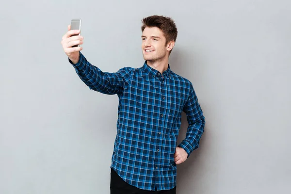 Wesoły, młody mężczyzna stojący szary mur i zrobić selfie — Zdjęcie stockowe