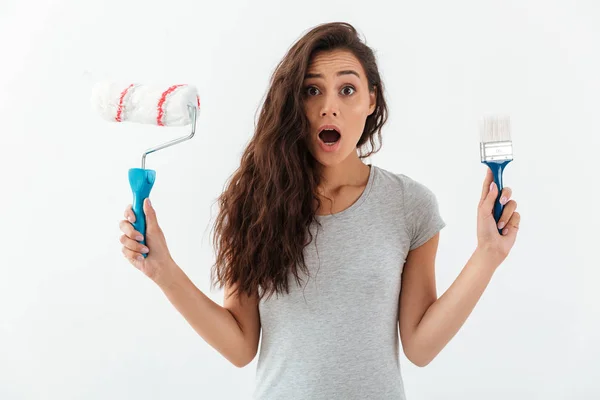 Amazed shocked young woman holding brush and paint roller — Stock Photo, Image