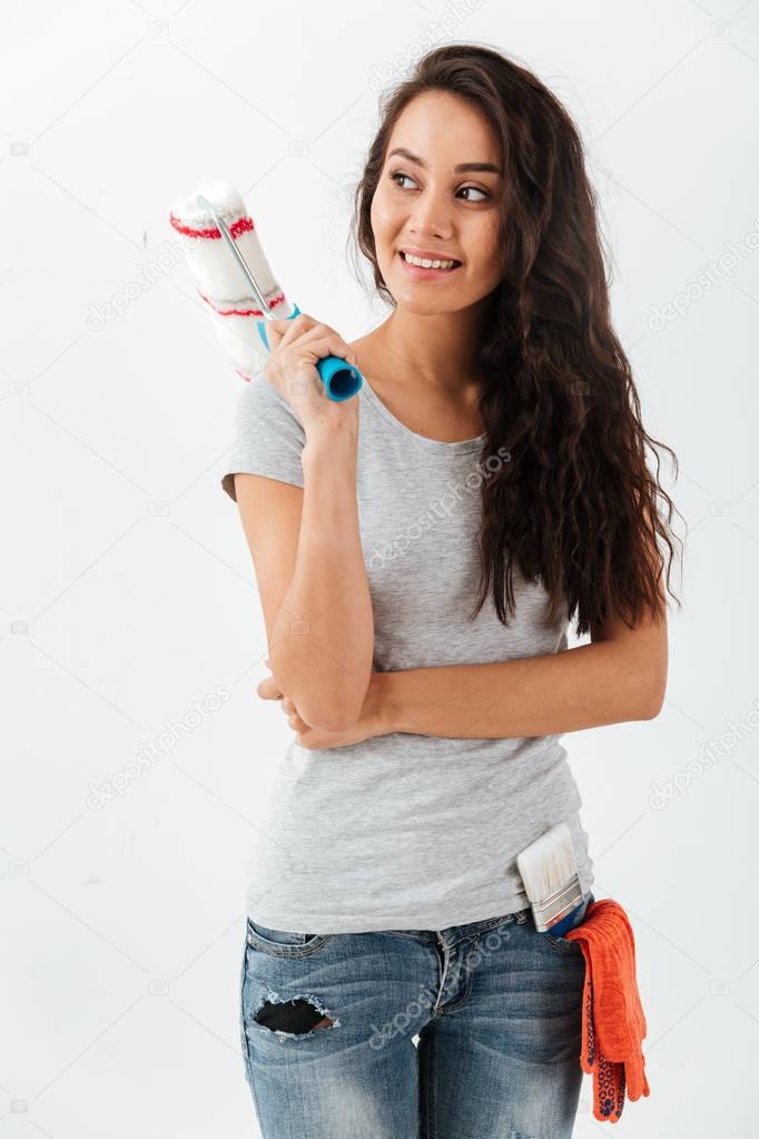 Cheerful beautiful young woman standing and holding paint roller