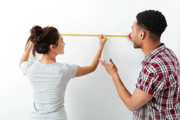 Feliz jovem casal de pé e usando fita métrica — Fotografia de Stock